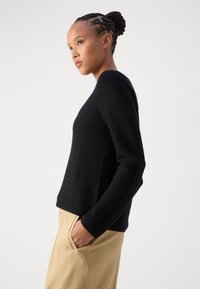 Schwarzer Strickpullover mit langen Ärmeln und rundem Halsausschnitt, im lässigen Schnitt und mit strukturiertem Stoff, kombiniert mit beigen Hosen.