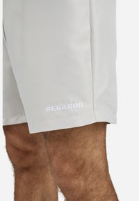 Pantalones cortos gris claro hechos de una tela suave y ligera que presentan un logotipo blanco "PEGADOR" visible en el dobladillo. Diseño simple y ajuste entallado.