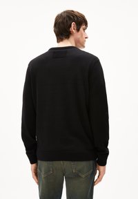 Schwarzer Strickpullover mit langen Ärmeln, gerippten Bündchen und einem runden Ausschnitt, von hinten dargestellt, mit einem strukturierten Etikett am Hals.