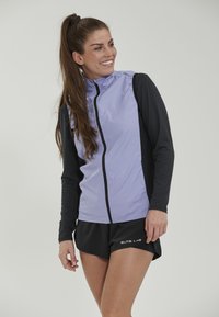 Lichtpaarse, ritssluitingjack met zwarte lange mouwen; heeft een strak ontwerp en ademende stof. Gecombineerd met zwarte shorts met logo.