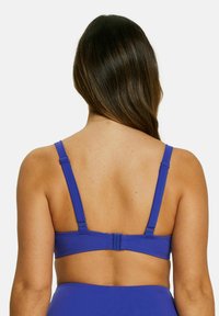 Haut de bikini bleu avec des bretelles réglables et un système de fermeture au dos. Texture lisse, design simple, mettant en avant une couleur bleu uni sans motifs.