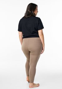 T-shirt nero a maniche corte abbinato a leggings beigi attillati e a vita alta. Texture liscia, design minimal e lunghezza alla caviglia.