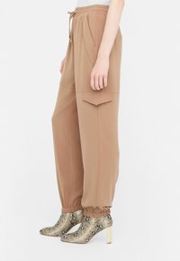Beige prodyšné kalhoty s elastickým pasem, bočními kapsami a volným střihem, doplněné vysokými hadími botami se vzorem.