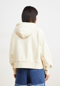 Cream-colored cropped hoodie with a hood, ribbed cuffs, and hem. Soft material and minimalist design, paired with denim shorts.