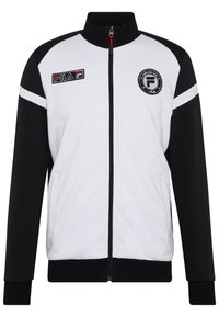 Giacca a zip bianca e nera con colletto alto, patch del logo Fila, strisce in contrasto e tasche laterali. Realizzata in un tessuto morbido.