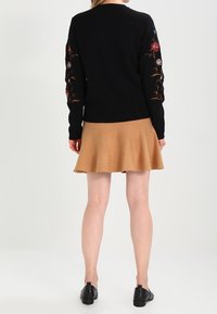Maglione nero a maglia con ricami floreali sulle maniche, abbinato a una gonna svasata color beige. Abbinato a scarpe in pelle nera.