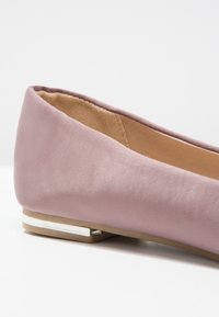Chaussure plate rose pâle avec doublure intérieure beige et petit talon carré agrémenté d'un accent métallique argenté, sur fond blanc.