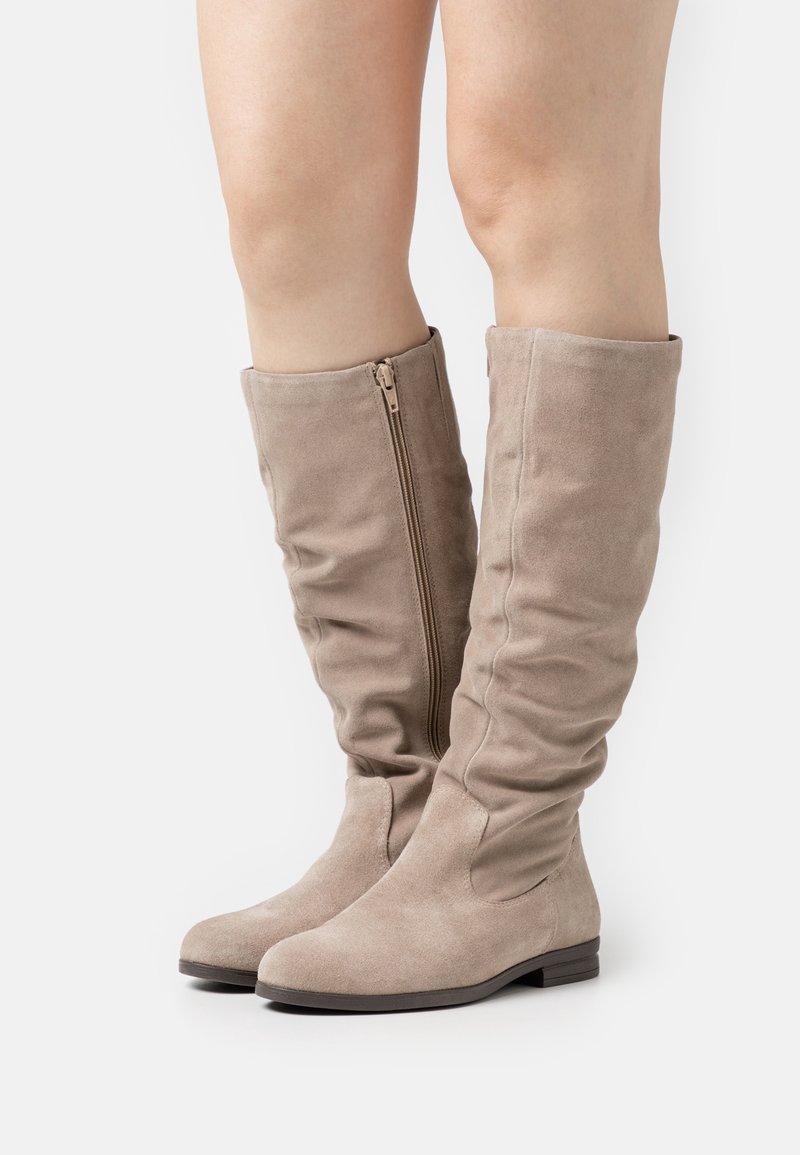 Bottes en suede beige à hauteur de genoux avec un design froncé, présentant une fermeture éclair sur le côté et une semelle plate. Texture lisse avec des accents minimes.