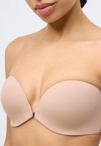 Σουτιέν χωρίς τιράντες σε φυσικό χρώμα, κατασκευασμένο από απαλό ύφασμα, με σχεδίαση χωρίς ραφές και κλείσιμο στο κέντρο με μεταλλικό κλιπ. Μαλακή υφή και διαμορφωμένα cups.