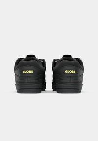 Czarne sneakersy z teksturowaną skórzaną wykończeniem, charakteryzujące się wyraźnym żółtym logo "GLOBE" na pięcie oraz wspierającym wykończeniem z tyłu cholewki.