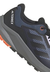 Czarno-szare buty sportowe z teksturowanym siateczkowym wierzchem, pomarańczowymi akcentami, wyraźnym trzy-pasowym wzorem i solidną szaro-rubberową podeszwą.