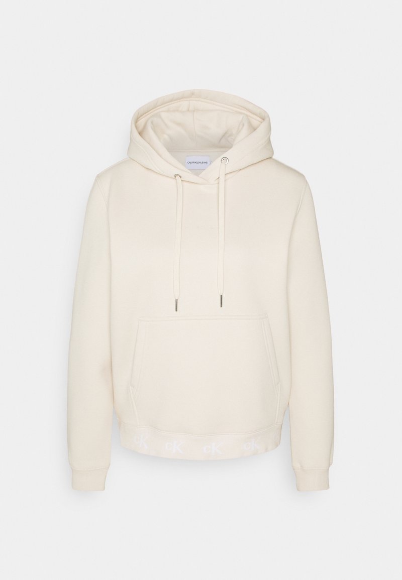 Sudadera color crema de tela suave, con un bolsillo frontal, cordones ajustables y una banda con logo a lo largo del dobladillo.