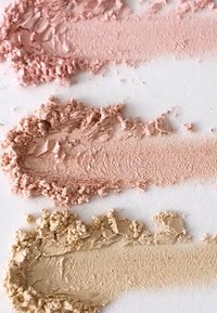 Tre svatches med pudder: toppen er lys rosa, midten er mørkere rosa, bunnen er beige. Hver har en teksturert, smuldrete utseende mot en hvit bakgrunn.