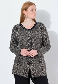 Czarny i beżowy kardigan w wzory z długimi rękawami, dekoltem w serek i zapięciem na guziki. Akcentowany jednolitym czarnym wykończeniem i teksturowanym materiałem.
