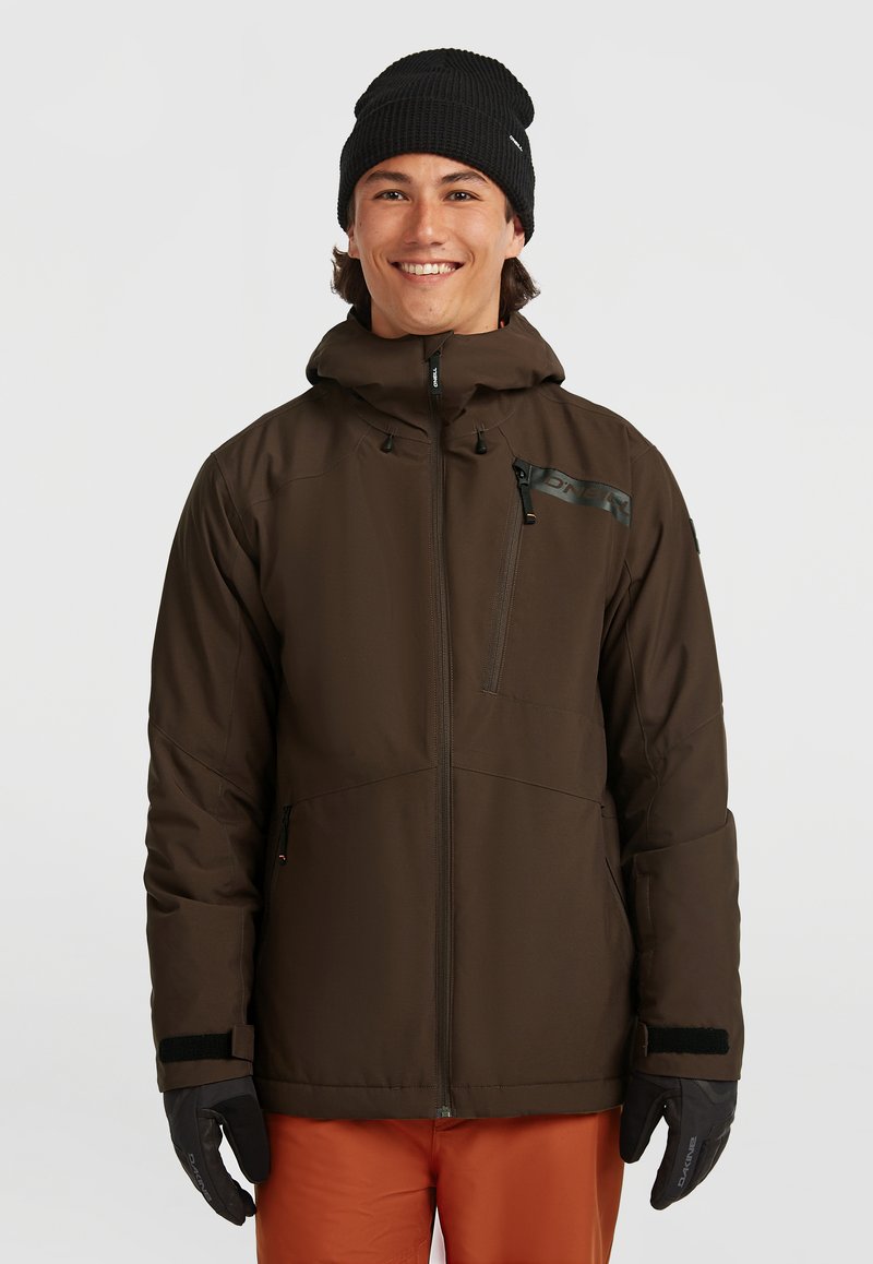 Bruine geïsoleerde jas met een hoge kraag, ritsvak op de borst en verstelbare manchetten, gecombineerd met oranje broek en zwarte handschoenen en muts.