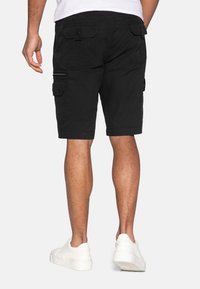 Shorts cargo noirs avec plusieurs poches, fabriqués dans un tissu durable. Présente une coupe décontractée et des baskets blanches contrastées.