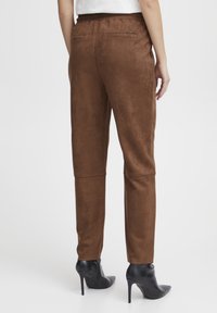 Brown suede-style pants with a relaxed fit, elastic waistband, and two back pockets, paired with black high-heeled boots.