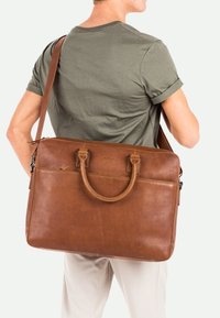 Valigia in pelle marrone con due manici e una tracolla removibile, caratterizzata da una texture liscia e un design minimalista.