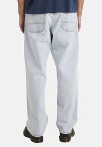 Lichtblauwe denim jeans met een relaxte pasvorm, voorzien van twee achterzakken, zichtbare stiksels en rechte pijpen, gecombineerd met zwarte laarzen.