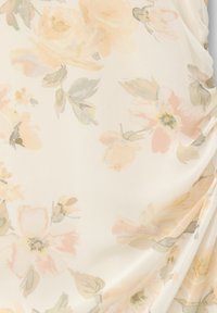 Tissu blanc transparent avec imprimé floral beige doux, pêche et vert clair et détail de volant froncé sur le côté.