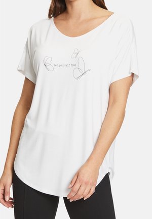 Vrouw draagt een wit loszittend T-shirt met korte mouwen, met drie eenvoudige vlinderlijntekeningen en de tekst "set yourself free" aan de voorkant.
