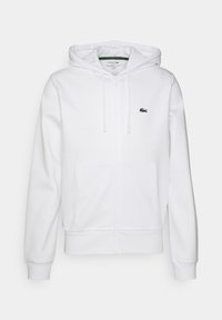 Vit zip-up huvtröja i mjukt material. Har en huva, framfickor och en liten grön broderad logotyp på vänster bröst.