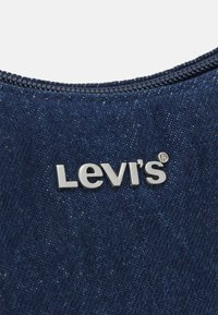 Tissu en denim Levi's de couleur bleu foncé avec une texture visible ; logo argenté centré. Motif de couture le long des bords. Détail de design classique.