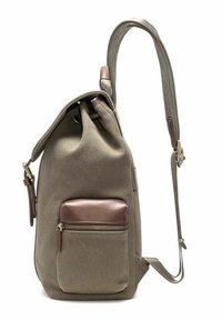 Torebka plecakowa w kolorze taupe z przednią kieszenią na zamek, ozdobiona brązowym skórzanym wykończeniem i regulowanymi ramiączkami na tle białym.
