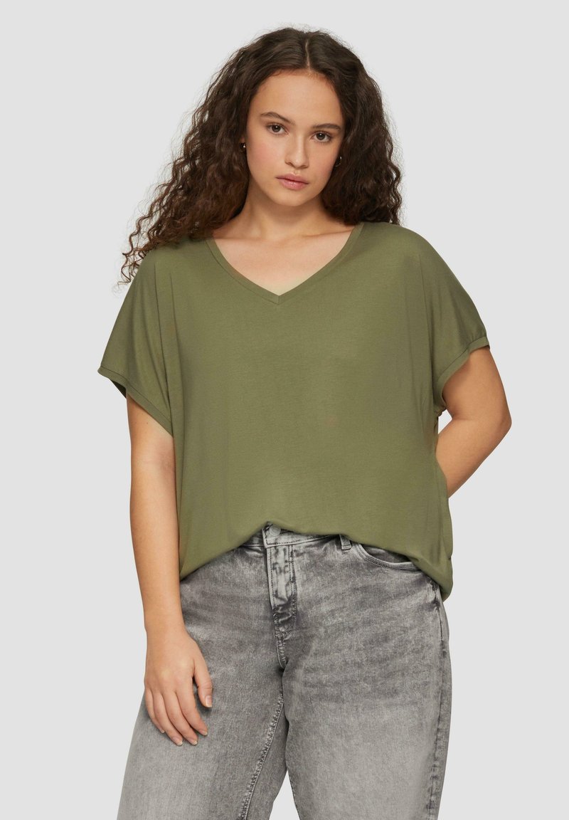 Olijfgroene V-hals top met korte mouwen, losse pasvorm en een zachte textuur, gecombineerd met grijze high-waisted jeans met een vervaagd patroon.