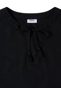 Encolure de blouse noire avec des cordons en tissu attachés se terminant par des pampilles, avec une petite étiquette blanche à l’intérieur du col.