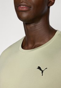 Lys grønn kortermet t-skjorte med rund hals og svart Puma-logo på brystet. Glatt tekstur med subtile detaljer rundt halslinningen.