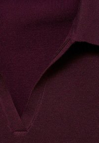Le pull en tricot bordeaux présente un design à col en V, une texture côtelée et des épaules sans couture. Matériau doux avec une finition lisse.