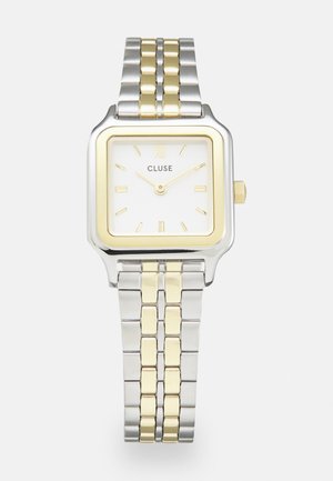 Relógio Cluse quadrado com um mostrador branco, detalhes em dourado e prateado, e uma bracelete bimetálica com elos alternados em dourado e prateado.