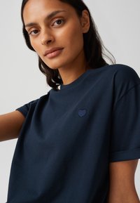 T-shirt di cotone blu navy con maniche corte, dotato di un piccolo cuore ricamato di colore blu scuro sul lato sinistro del petto.