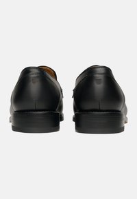 Scarpe nere in pelle con retro arrotondato, texture liscia e tacco basso impilato. Dettaglio del logo discreto vicino al tacco.