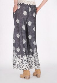Wijde broek van donkergrijze stof, met witte bloemenpatronen, een kant tailleband en een decoratieve witte rand aan de zoom.