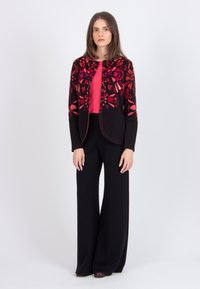 Red floral-embroidered black cardigan with a rounded neckline, paired with a solid red top, and black wide-leg pants. Smooth texture throughout.
