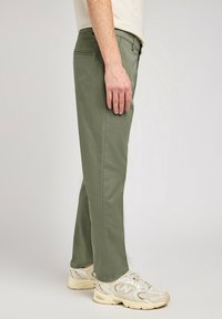 Olivgröna, raka byxor med en slät textur, med en framficka och en sidoseam. Kombineras med beige sportskor.