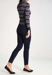 Haut à rayures marines à manches longues avec des fils argentés, pantalon foncé ajusté et ballerines noires. Le haut présente des rayures horizontales multicolores.