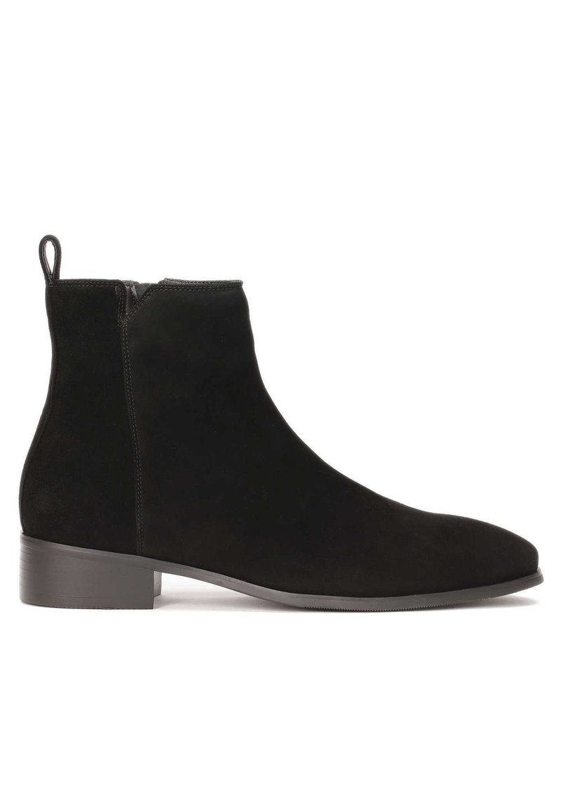 Botines de ante negro con una textura suave, puntera redonda y un tacón bajo apilado. Presentan un cierre de cremallera lateral y una pestaña en la parte posterior.