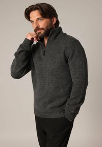 Pull en maille gris foncé avec un col montant et un zip mi-long. Manches et bas côtelés, tissu texturé avec un aspect doux.