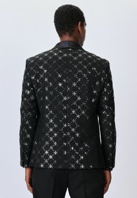 Fekete flitteres blézer gyémántmintával, texturált felülettel és kontrasztos fekete gallérral. Feszes fazonú, gombos mandzsettákkal.