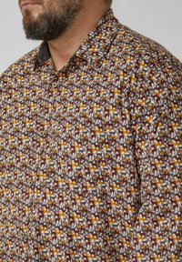 Brązowa koszula zapinana na guziki z powtarzającym się wzorem stylizowanych zwierząt w kolorach żółtym, białym i szarym na teksturowanym tle.