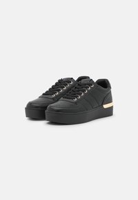 Black platform sneakers with a textured upper, lace closure, gold eyelets, and a metallic accent on the heel. Smooth black sole.