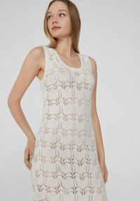 Weißes gestricktes Kleid mit U-Boot-Ausschnitt und ärmellosem Design. Es hat ein Spitzenmuster und eine figurbetonte Silhouette.