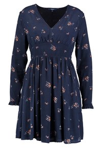 Robe bleu marine à manches longues avec un col en V, une taille froncée et un petit imprimé floral orange et blanc dispersé sur le tissu.