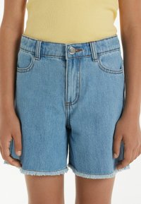 Shorts en denim bleu clair avec un ourlet effiloché, dotés d'une fermeture à bouton en métal, de poches avant et de détails de couture en contraste.