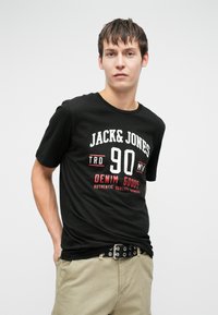 Tricou din bumbac negru, cu un imprimeu grafic în text alb și roșu, cu „JACK & JONES” și „DENIM GOODS”. Guler rotund, mâneci scurte.