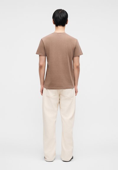 Καφέ βαμβακερό t-shirt με κοντά μανίκια και στρογγυλή λαιμόκοψη, σετάρισμένο με φαρδιά κρεμ παντελόνια και μαύρα παπούτσια.