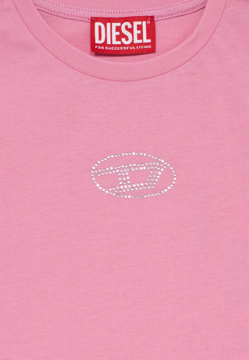 T-shirt in cotone rosa con collo rotondo, caratterizzato da un design con logo in strass argentati al centro. L'etichetta riporta "DIESEL" in rosso.